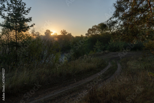 Autumn time. Dawn over the river in a misty  brooding haze. Beautiful view of the forest and river  covered with fog in the early morning. The sun s rays of light.