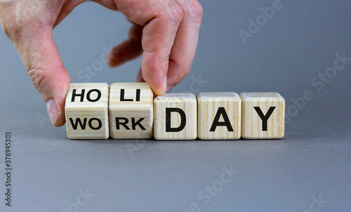 Hand turns a cube and changes the expression 'workday' to 'holiday'. Beautiful grey background, copy space. Concept.