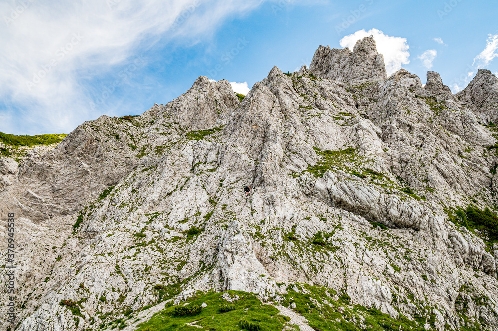 Young woman summer hiker with backpack climbing metal cables huge limestone rock wall via ferrata. Female trekker in challenging terrain Karavanke mountains, Slovenia, Karawanken, Carinthia, Austria Young woman summer hiker with backpack climbing metal cables huge limestone rock wall via ferrata. Female trekker in challenging terrain Karavanke mountains, Slovenia, Karawanken, Carinthia, Austria