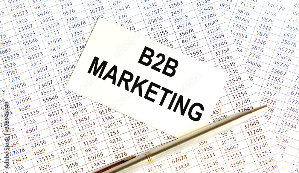 B2B MARKETING is on the business card. Nearby is a pen, reports and books. B2B MARKETING is on the business card. Nearby is a pen, reports and books.