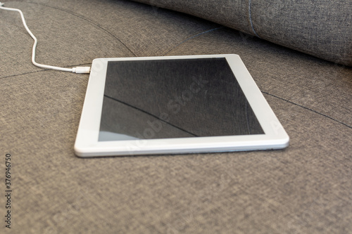 A white tablet charging energy on the sofa. blur background with copy space