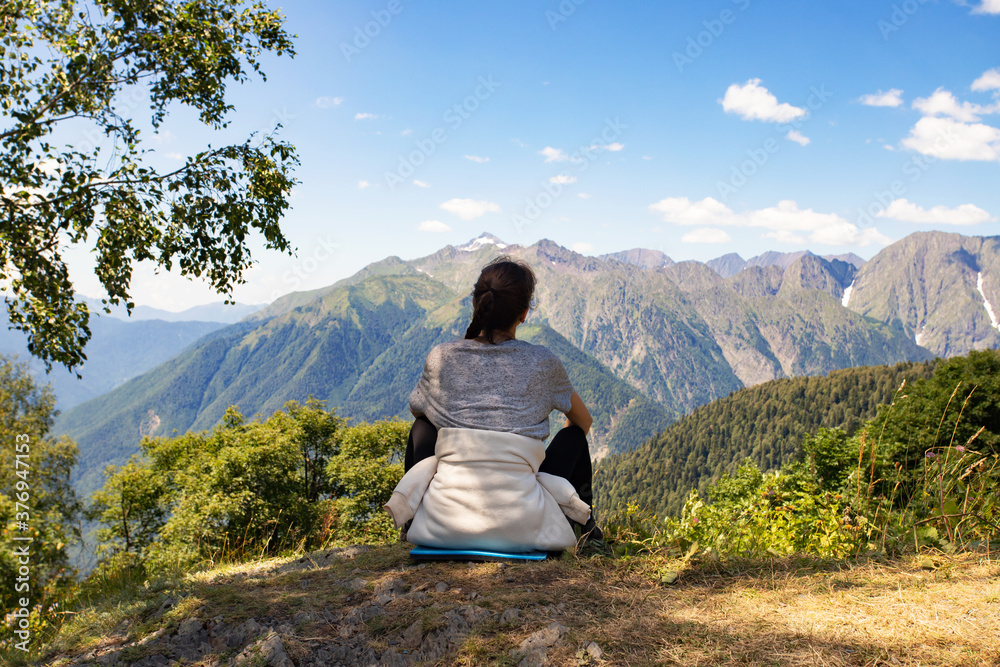 Girl in the mountains looking at the landscape, sitting on top, view from the back