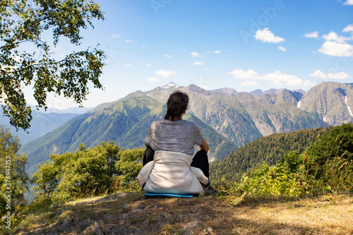 Girl in the mountains looking at the landscape  sitting on top  view from the back