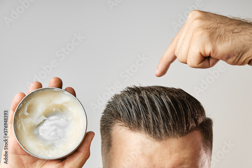Fotografie Man applying a clay, pomade, wax, gel or mousse from round metal box for styling his hair after barbershop hair cut