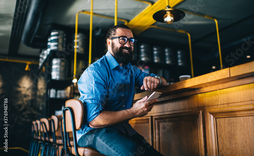 Bilde på lerret Cheerful bearded 40 man in casual wear holding mobile phone making banking onlin