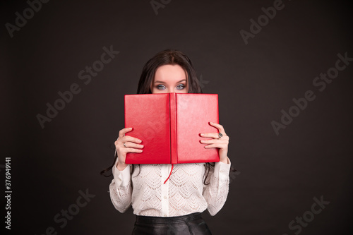Portrait of a business woman student closes her face with a daily on a black background © fasli
