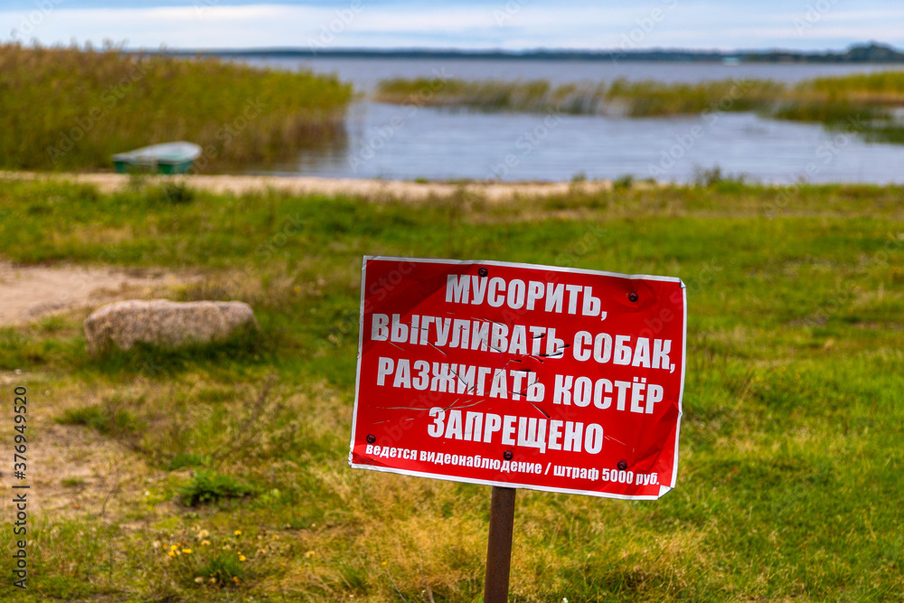 Warning red sign on the background of the lake. Translation: Littering, walking dogs, lighting a fire is FORBIDDEN.