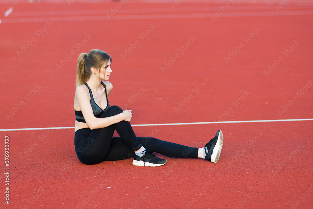A female coach with dark hair stands on the red running track of the stadium