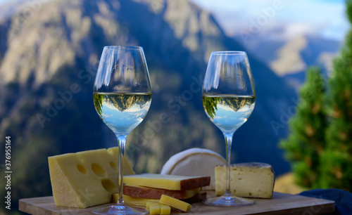 Tasty cheese and wine from Savoy region in France, beaufort, abondance, emmental, tomme and reblochon de savoie cheeses and glass of white wine served outdoor with Alpine mountains peaks on background photo