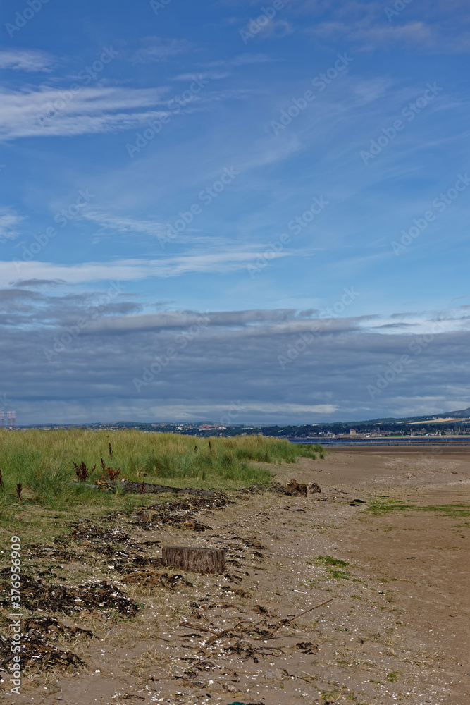 The High Tide line of Shell and seaweed debris against the small grass covered undulating dues of the Tay Estuary at Low tide in August.