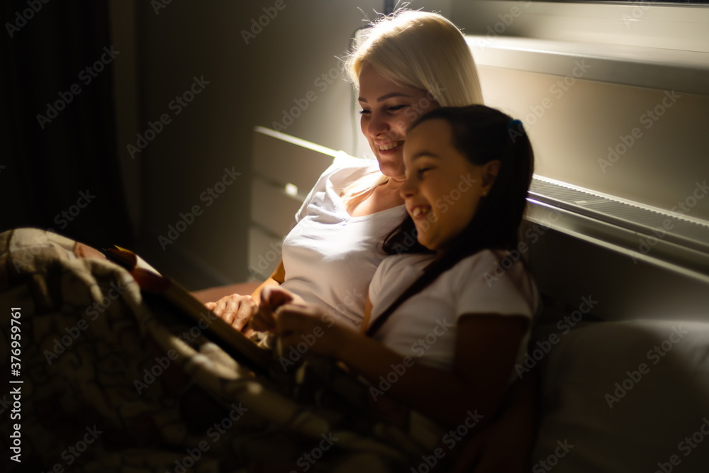 happy family mother and daughter read a book in the evening at home