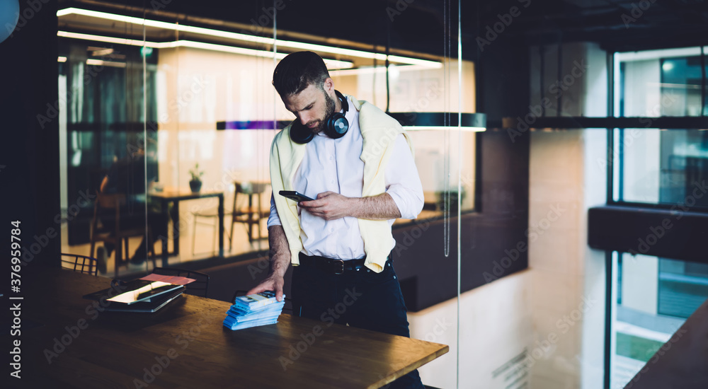 Successful businessman with smartphone standing near table in modern workspace Successful businessman with smartphone standing near table in modern workspace