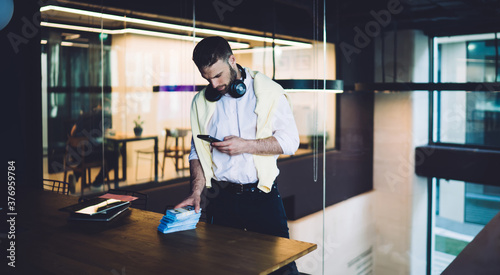 Successful businessman with smartphone standing near table in modern workspace © BullRun