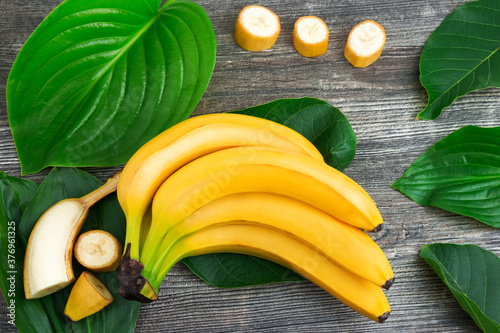 Bunch of raw organic yellow bananas with slices and green leaves on wooden background
