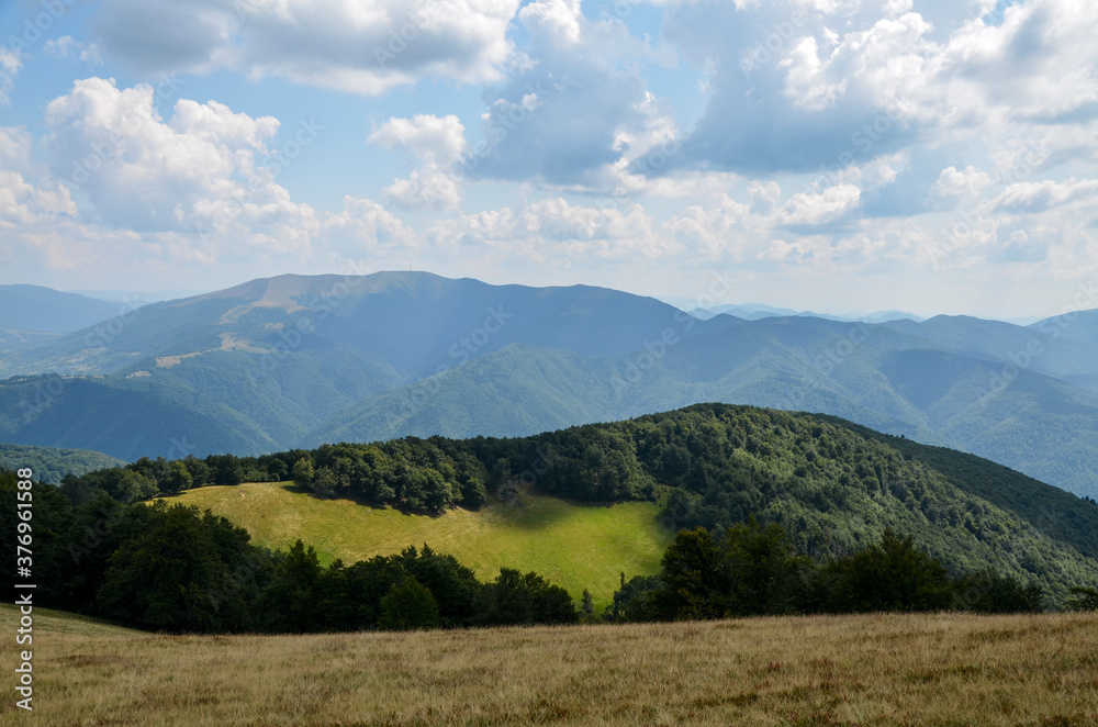 Beautiful summer mountain landscape. lit by the sun green forests on the hills under blue sky with clouds. Carpathians, Ukraine