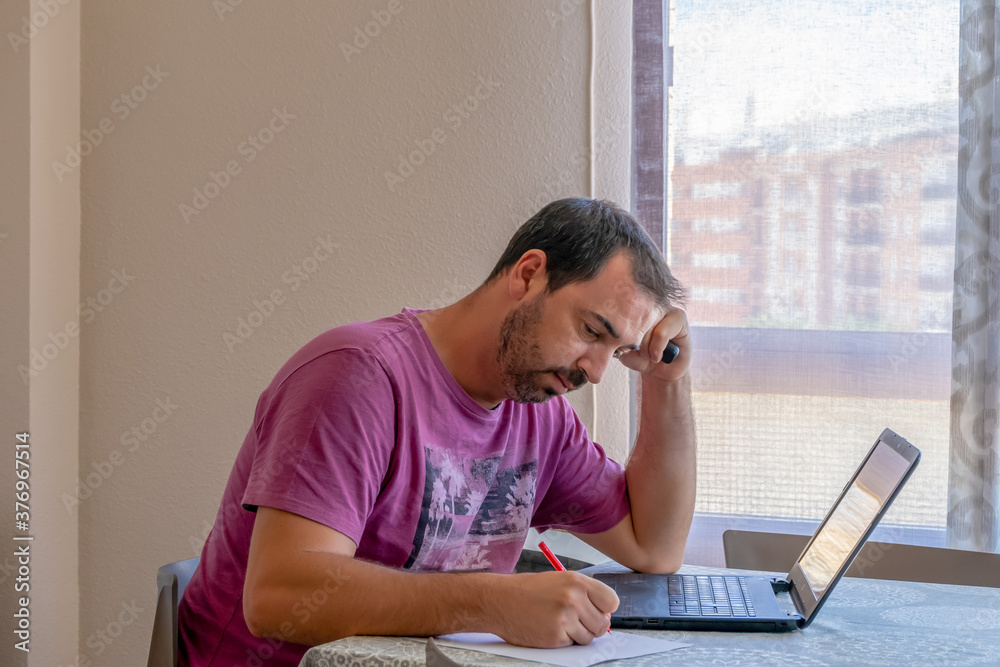 Worried bearded man dressed in a purple t-shirt looking at the laptop Worried bearded man dressed in a purple t-shirt looking at the laptop