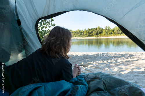 close up image of young female lies in the tent and looks at the beautiful river out from the open window. Camping in beautiful places, active and healthy lifestyle. © Anna