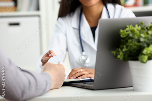 Female physician hand give white blank calling card to businesswoman closeup in office. Physical disease prevention examine patient instrument shop healthy lifestyle family doctor concept