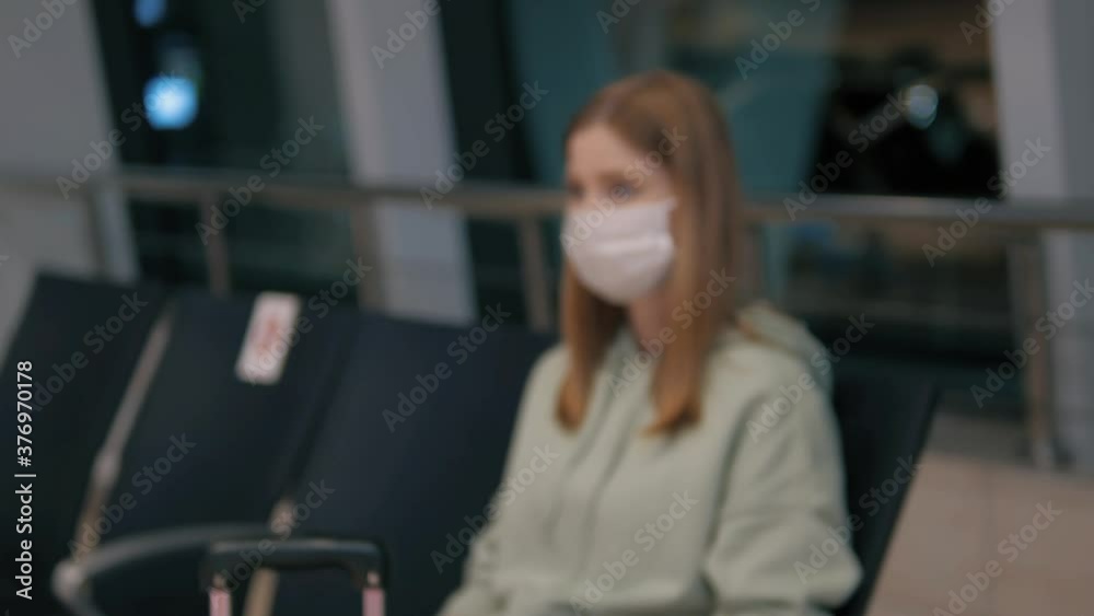 Young female wearing protective gloves and mask waiting with her luggage at the airport or railway station having social distance . Safe travels during coronavirus, empty airport Young female wearing protective gloves and mask waiting with her luggage at the airport or railway station having social distance . Safe travels during coronavirus, empty airport