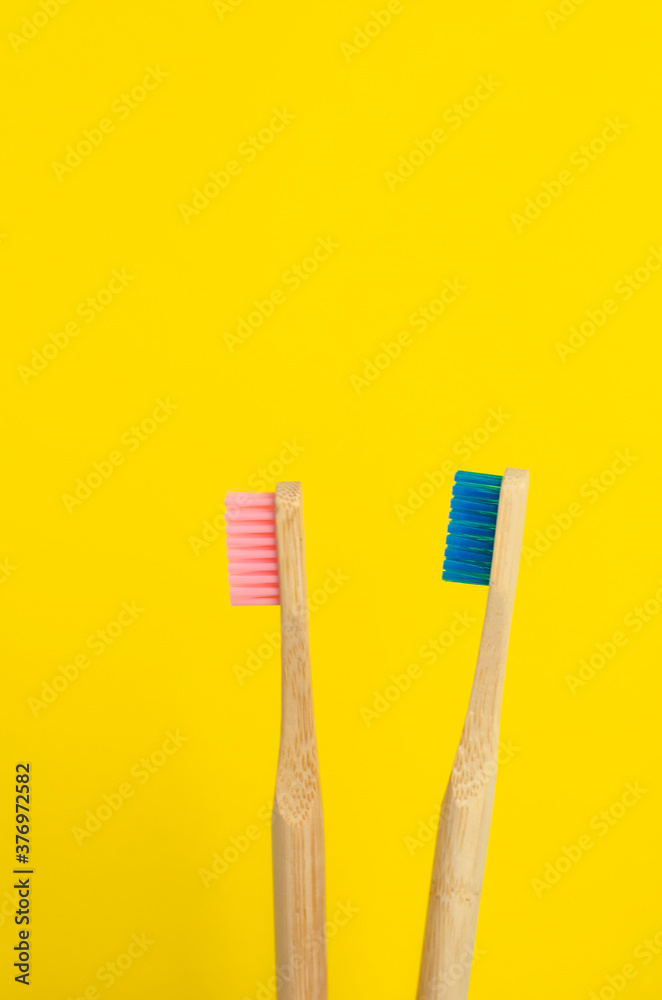 dos cepillos de dientes uno rosa y otro azul de bambú con fondo liso de color amarillo dos cepillos de dientes uno rosa y otro azul de bambú con fondo liso de color amarillo