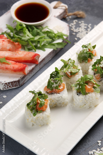 Japanese cuisine. Rice rolls with red fish, arugula and crab meat with soy sauce on a white plate on a gray background. Background image, copy space