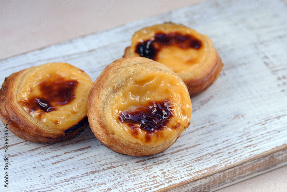 Traditional Portuguese popular dessert Pastel de nata or Pastel de Belem on a white wooden board. Delicious puff pastry cups with custard. Gastronomic travel in Portugal. Traditional Portuguese popular dessert Pastel de nata or Pastel de Belem on a white wooden board. Delicious puff pastry cups with custard. Gastronomic travel in Portugal.