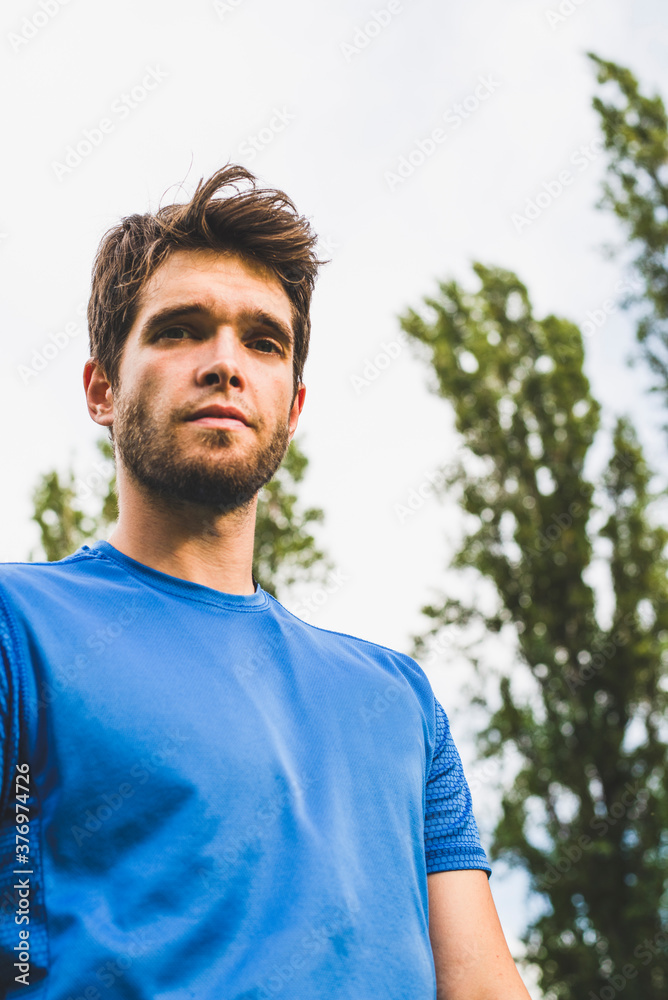 Close-up of attractive young man with beard dressed in sportswear and with trees behind looking at camera. Close-up of attractive young man with beard dressed in sportswear and with trees behind looking at camera.