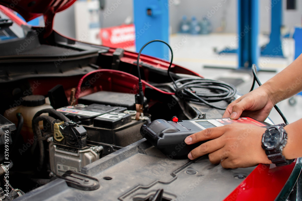 A mechanic uses a device to check the voltage of the car battery.