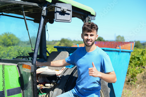 handsome young man winemaker driving tractor trailer in his vineyard during wine harvest