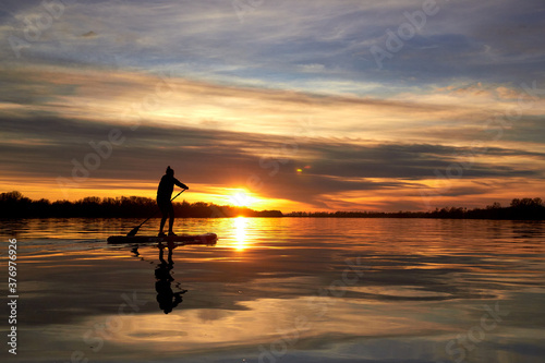 Silhouette of woman paddle on SUP  stand up paddle board  on quiet river at dusk. Winter sport