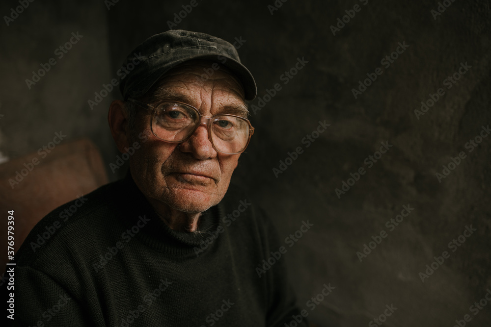 Pensive old man in glasses with gray hair looks away. wrinkles. wisdom. against a dark gray texture wall. bald head. in a knitted sweater. Portrait.