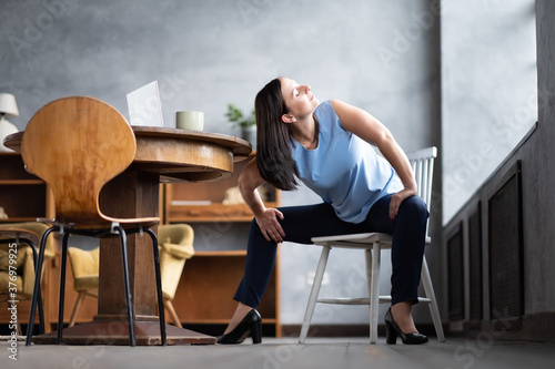 Caucasian girl workout doing Goddess Pose temple or sumo pose, stupasana, using chair sitting at home, living room. photo