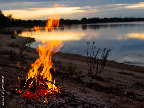 Fire on a sandy beach, large flames on the background of a lake and forest. night sky. outdoor recreation concept