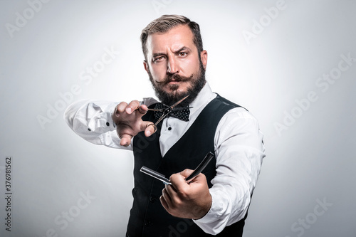 Barber with straight razor and scissors over grey background. Brutal man holding proffecional tools. Barber shop. Mens haircut