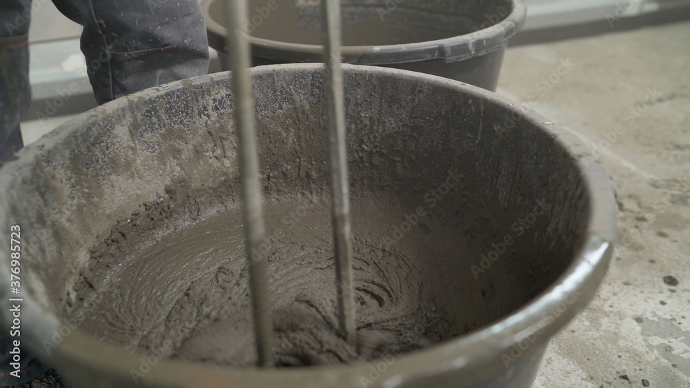 Fototapeta premium The mortar is mixed in a bucket. Floor repair. Mixing of building floor mortar. mixing cement in the bucket mixer with the trowel at the side work, Construction work