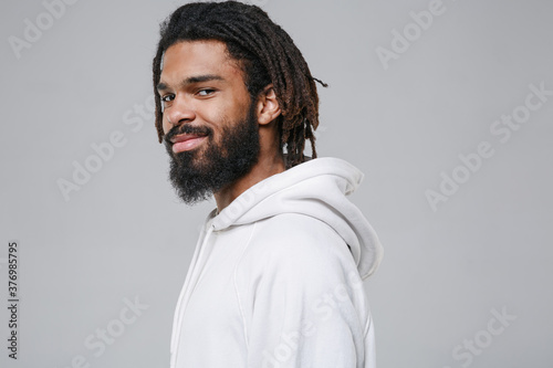 Valokuva Side view of smiling handsome young african american man guy with dreadlocks 20s wearing white casual streetwear hoodie posing looking camera isolated on grey color wall background studio portrait