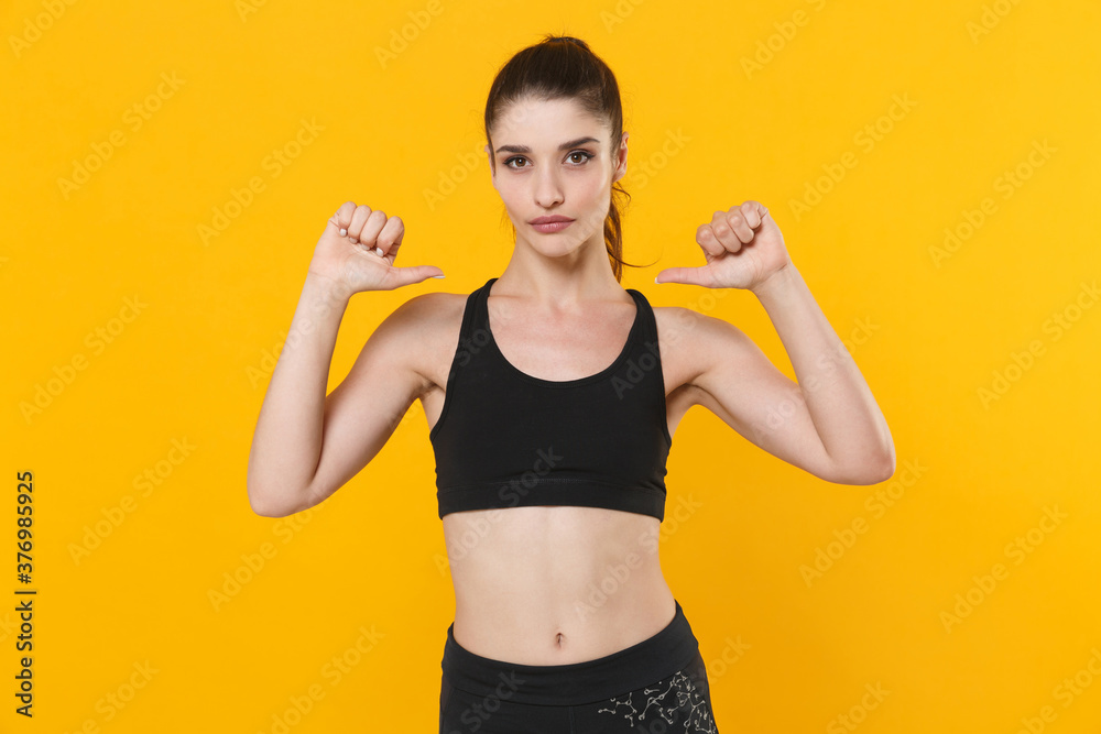 Attractive young fitness sporty woman 20s wearing black sportswear posing training working out pointing thumbs on herself looking camera isolated on bright yellow color background studio portrait. Attractive young fitness sporty woman 20s wearing black sportswear posing training working out pointing thumbs on herself looking camera isolated on bright yellow color background studio portrait.