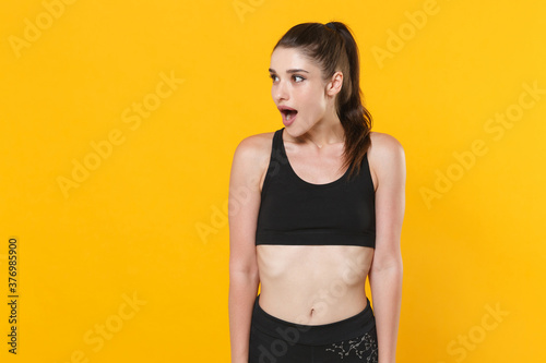 Shocked amazed young fitness sporty woman 20s wearing black sportswear posing working out training keeping mouth open looking aside isolated on bright yellow color wall background studio portrait. © ViDi Studio