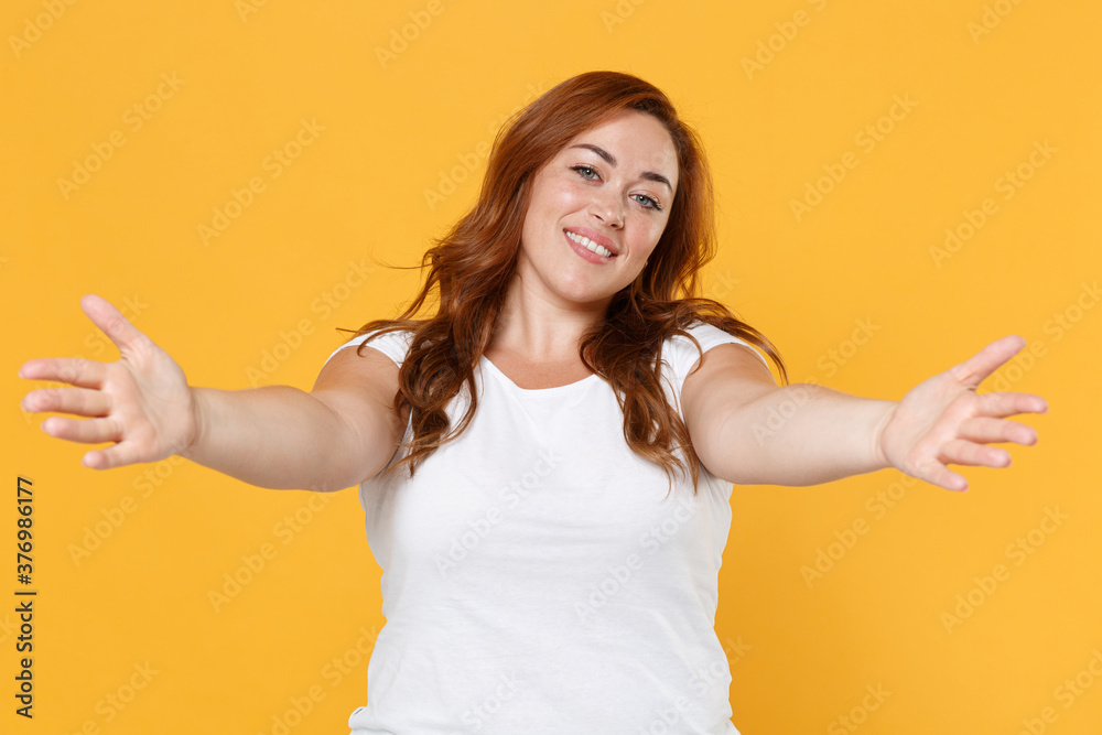 Smiling young redhead plus size body positive female woman girl 20s in white blank design casual t-shirt posing reach out stretch hands for hugs isolated on yellow color background studio portrait. Smiling young redhead plus size body positive female woman girl 20s in white blank design casual t-shirt posing reach out stretch hands for hugs isolated on yellow color background studio portrait.