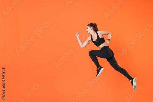 Full length side view of portrait of young fitness sporty woman 20s wearing black sportswear posing training working out jumping like running looking aside isolated on orange color background studio.