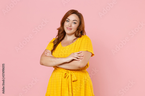 Cuadro en lienzo Smiling beautiful young redhead plus size body positive female woman girl 20s in yellow dress posing holding hands crossed looking camera isolated on pastel pink color wall background studio portrait