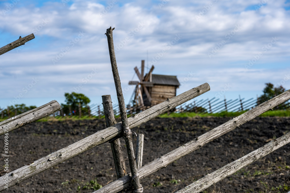 vintage wooden mill behind a fence on a green hill against a blue sky background