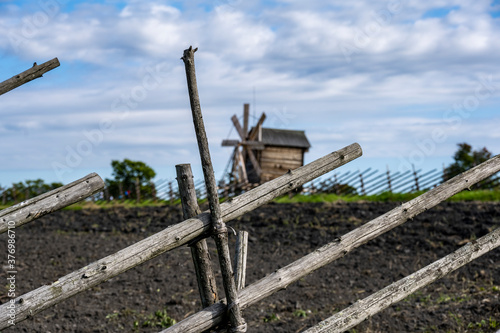 vintage wooden mill behind a fence on a green hill against a blue sky background