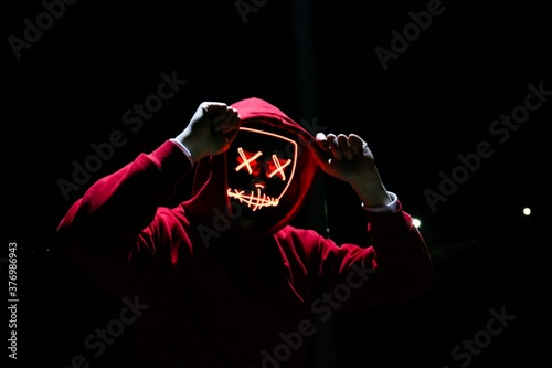 A Man Wearing A Red Hoodie With Red Glowing Mask In The Dark Backgroun photo