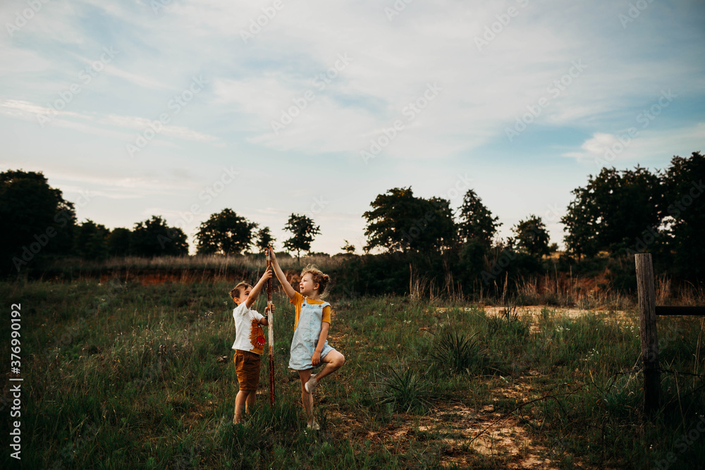 Brother and sister standing in open field at sunset Brother and sister standing in open field at sunset