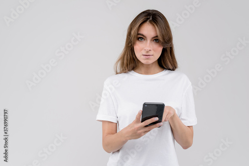 Young woman holding a smartphone standing on white background