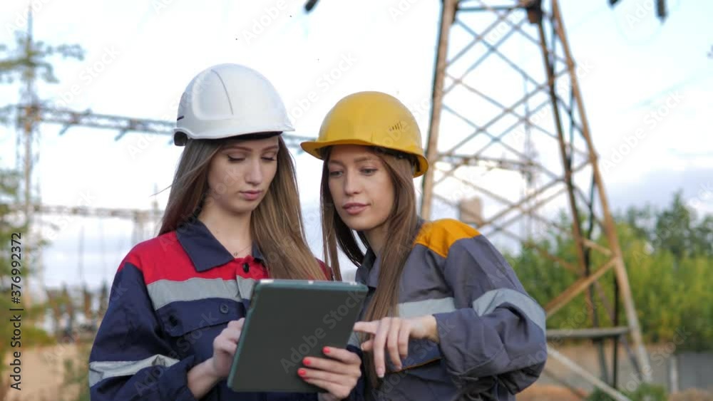 Two women energy workers conducts an inspection of equipment and power lines Two women energy workers conducts an inspection of equipment and power lines