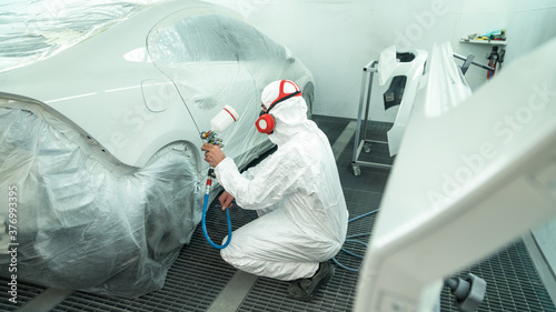 Automobile painting. Car painter with gun in chamber. Spray operation. 