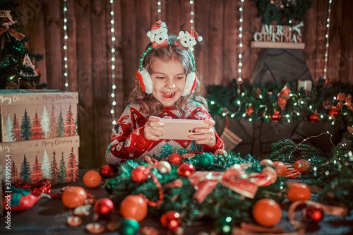 Girl using phone near Christmas tree in the decorative interior. Christmas and New Year photo.