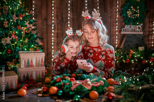 Mother and daughter looking the phone next to the christmas tree and shopping online.